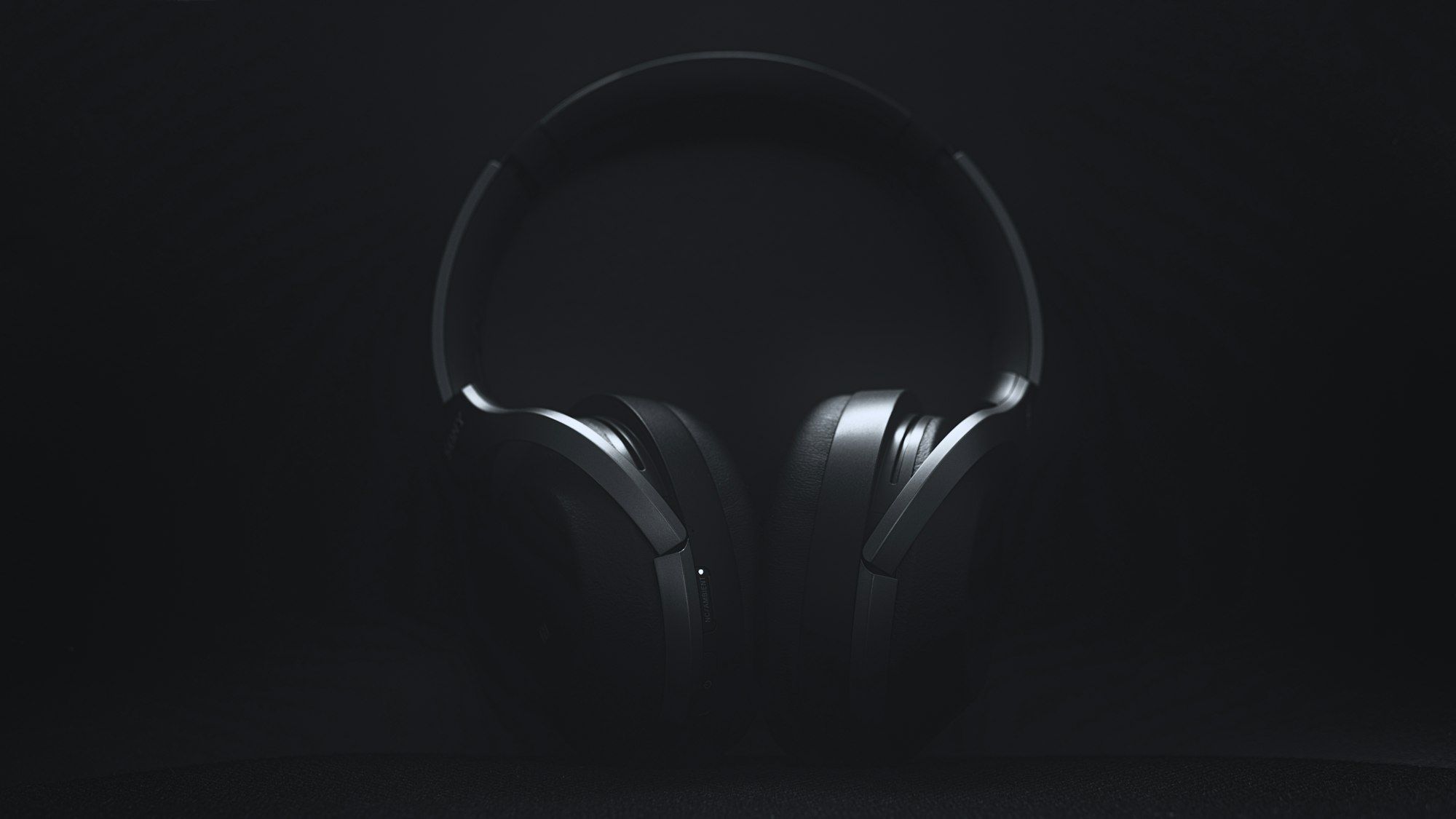 Black over-ear HELM headphones emerging from deep shadow, ultra-moody near-black background