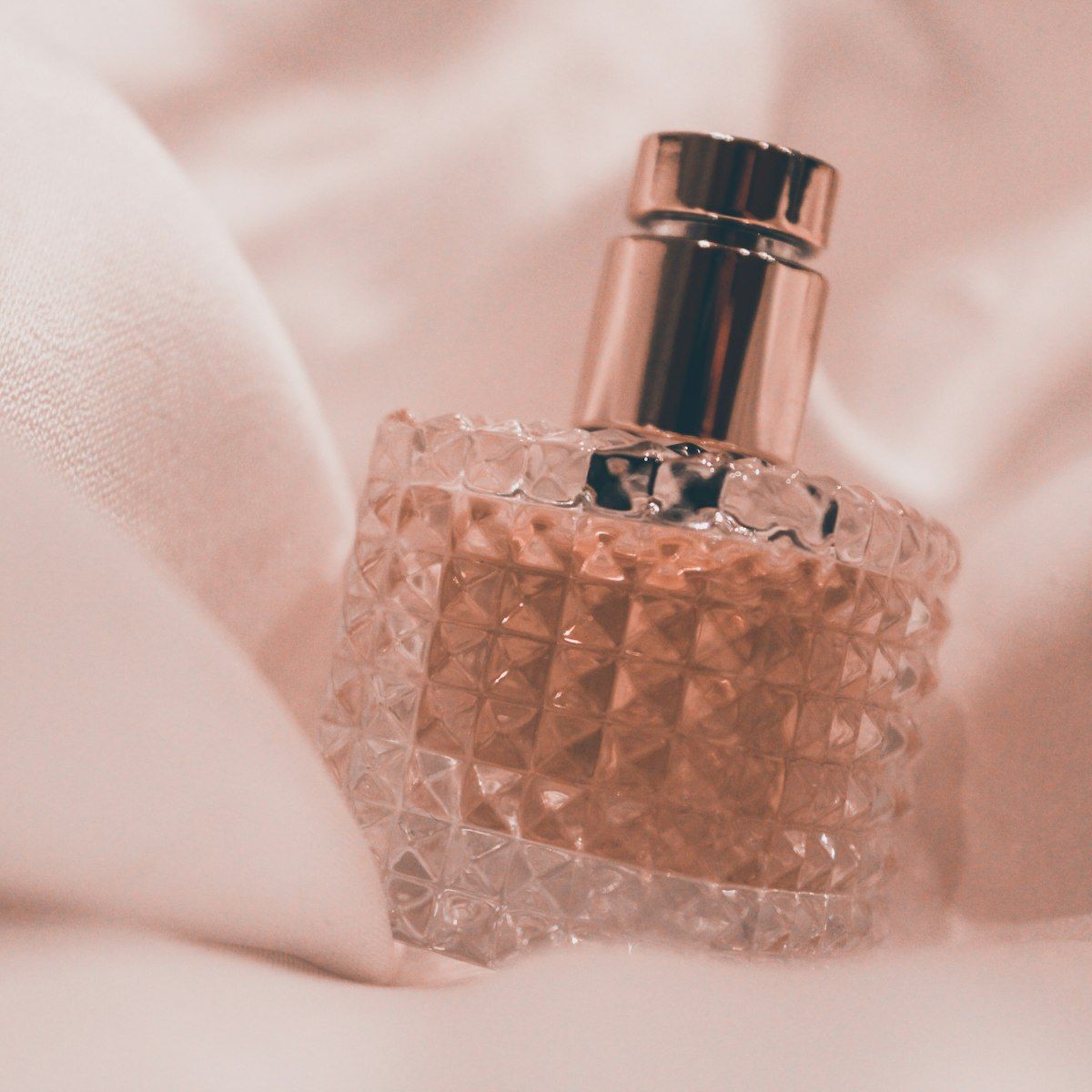 Perfume bottle on white silk in soft pink light