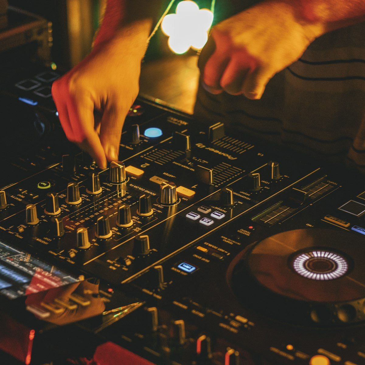 Close-up of a DJ's hands working an illuminated mixing console