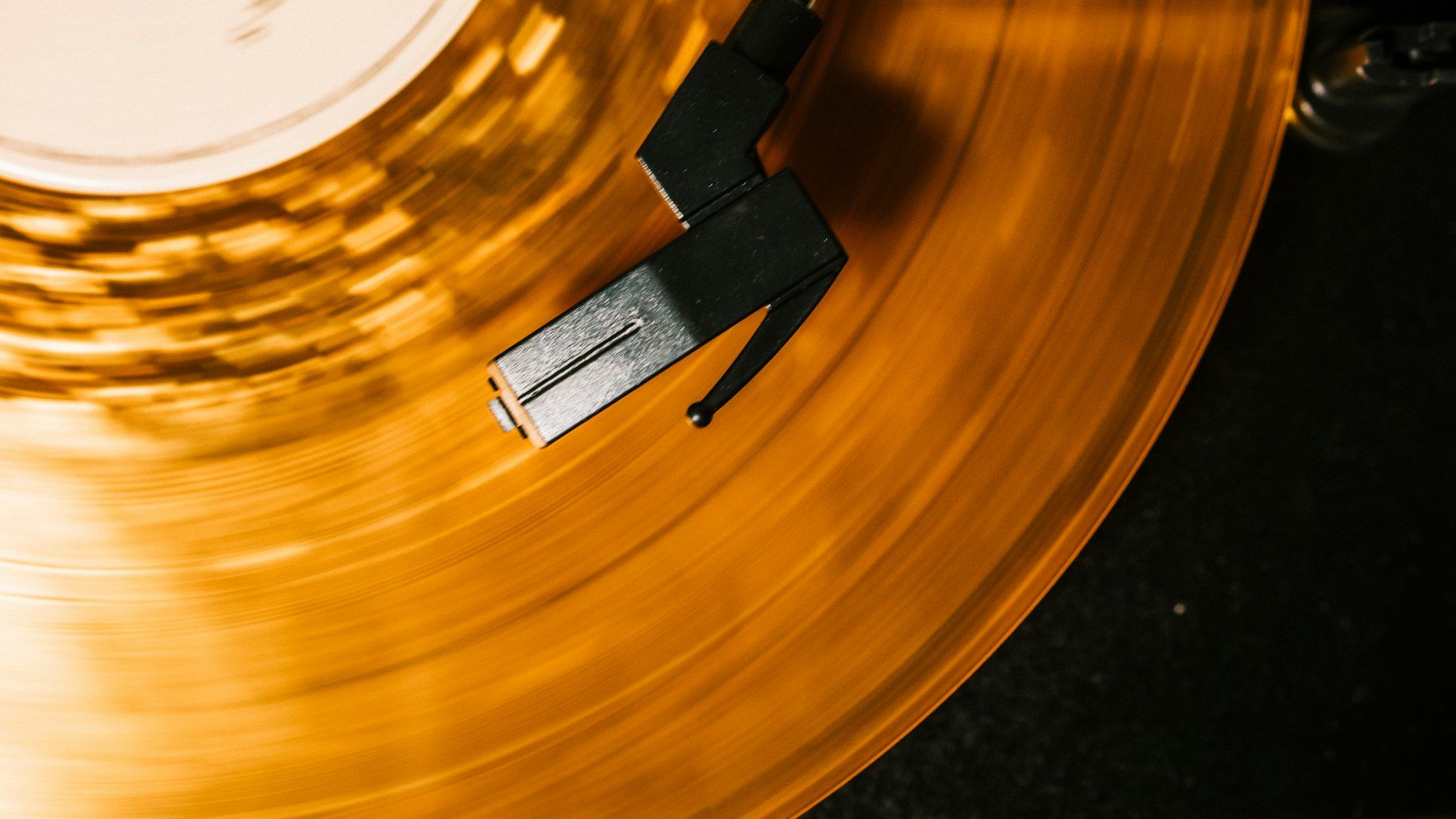 Close-up of an amber translucent vinyl record under a tonearm, lit by a warm golden glow