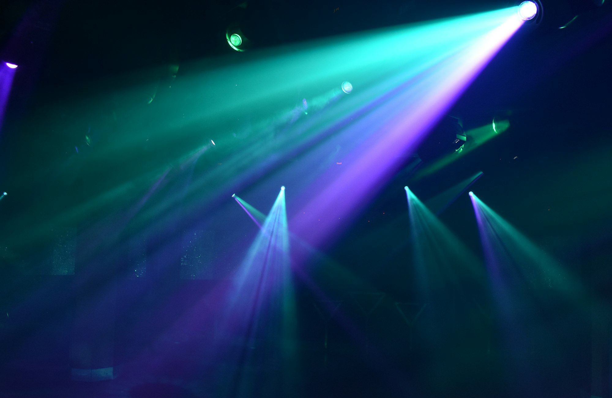 Teal and purple stage beams cutting across a dark concert venue